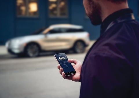 A person is shown interacting with a smartphone to connect to a Lincoln vehicle across the street. | Dave Sinclair Lincoln St. Peters in Saint Peters MO