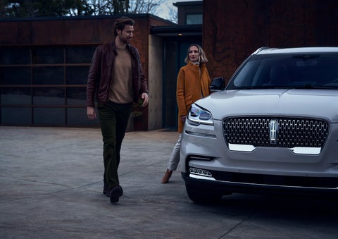 A man and a woman approaching a 2024 Lincoln Aviator® SUV, which illuminates certain lights when they are close | Dave Sinclair Lincoln St. Peters in Saint Peters MO