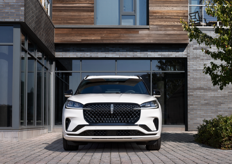 A white 2025 Lincoln Aviator® SUV is shown parked outside a modern building with gray brick and wood accents. | Dave Sinclair Lincoln St. Peters in Saint Peters MO