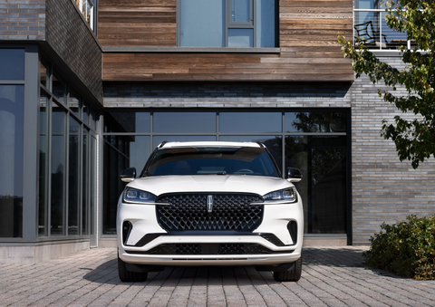 A white 2025 Lincoln Aviator® SUV is shown parked outside a modern building with gray brick and wood accents. | Dave Sinclair Lincoln St. Peters in Saint Peters MO