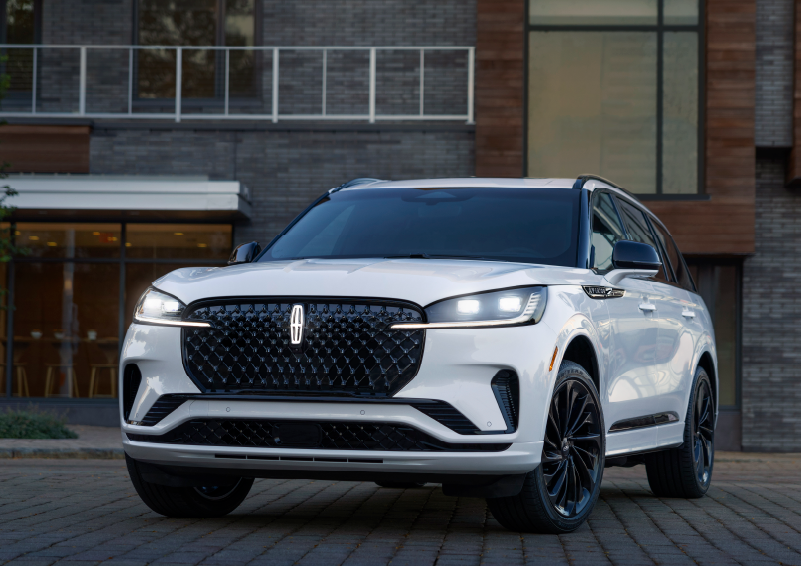 A white 2025 Lincoln Aviator® SUV is shown parked outside a modern building with gray brick and wood accents. | Dave Sinclair Lincoln St. Peters in Saint Peters MO