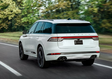 A white 2026 Lincoln Aviator® SUV is being driven away down a road lined with colorful trees. | Dave Sinclair Lincoln St. Peters in Saint Peters MO