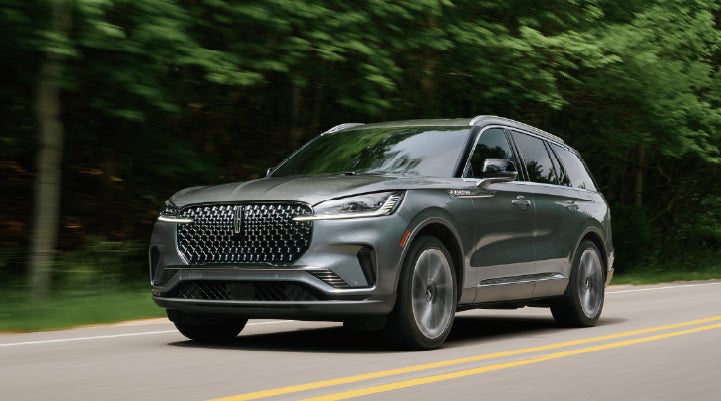 A 2027 Lincoln Aviator® SUV is being driven down a road lined with trees. | Dave Sinclair Lincoln St. Peters in Saint Peters MO