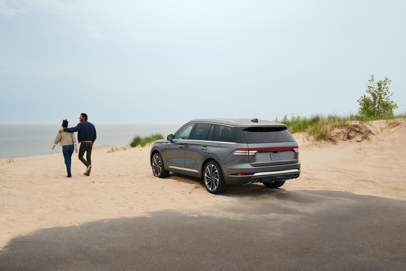 Couple walking on a sandy lake beach beside a parked Lincoln Aviator