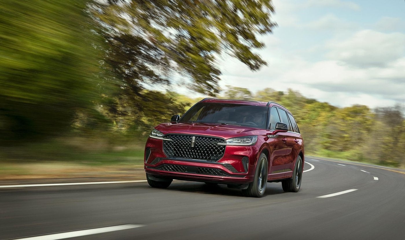 Red Lincoln Aviator driving on a curving country road lined with trees