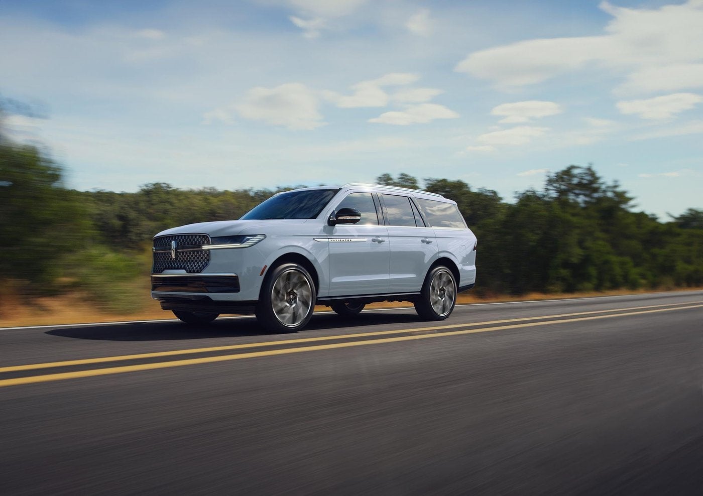 White Lincoln Navigator driving on a two lane highway under a blue sky