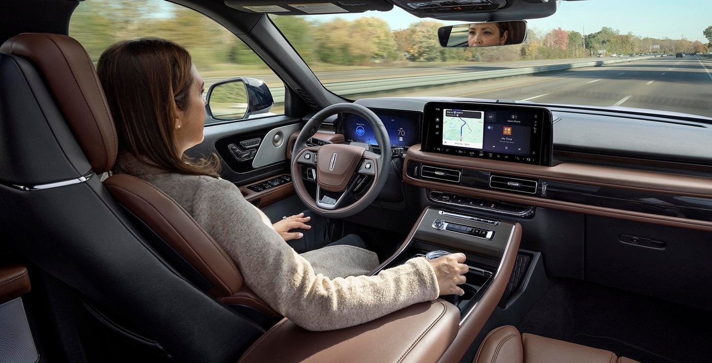 Woman driving a Lincoln Aviator on the highway with the touchscreen lit