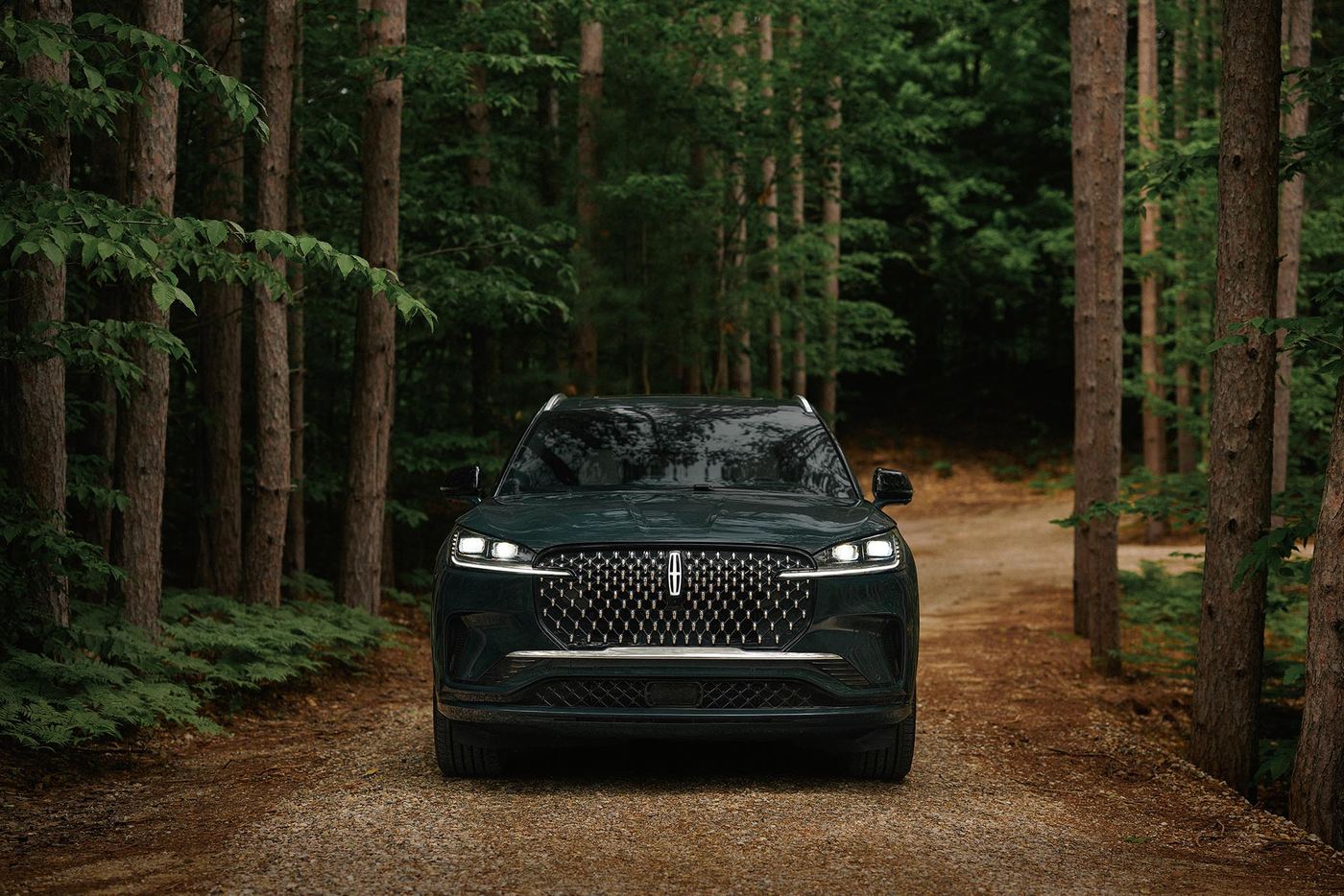 Dark green Lincoln Aviator with headlights on driving a gravel forest road