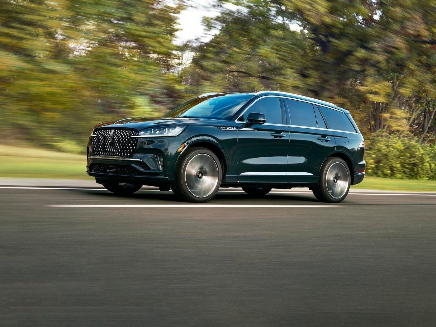 Dark green Lincoln Aviator driving on a road past blurred trees