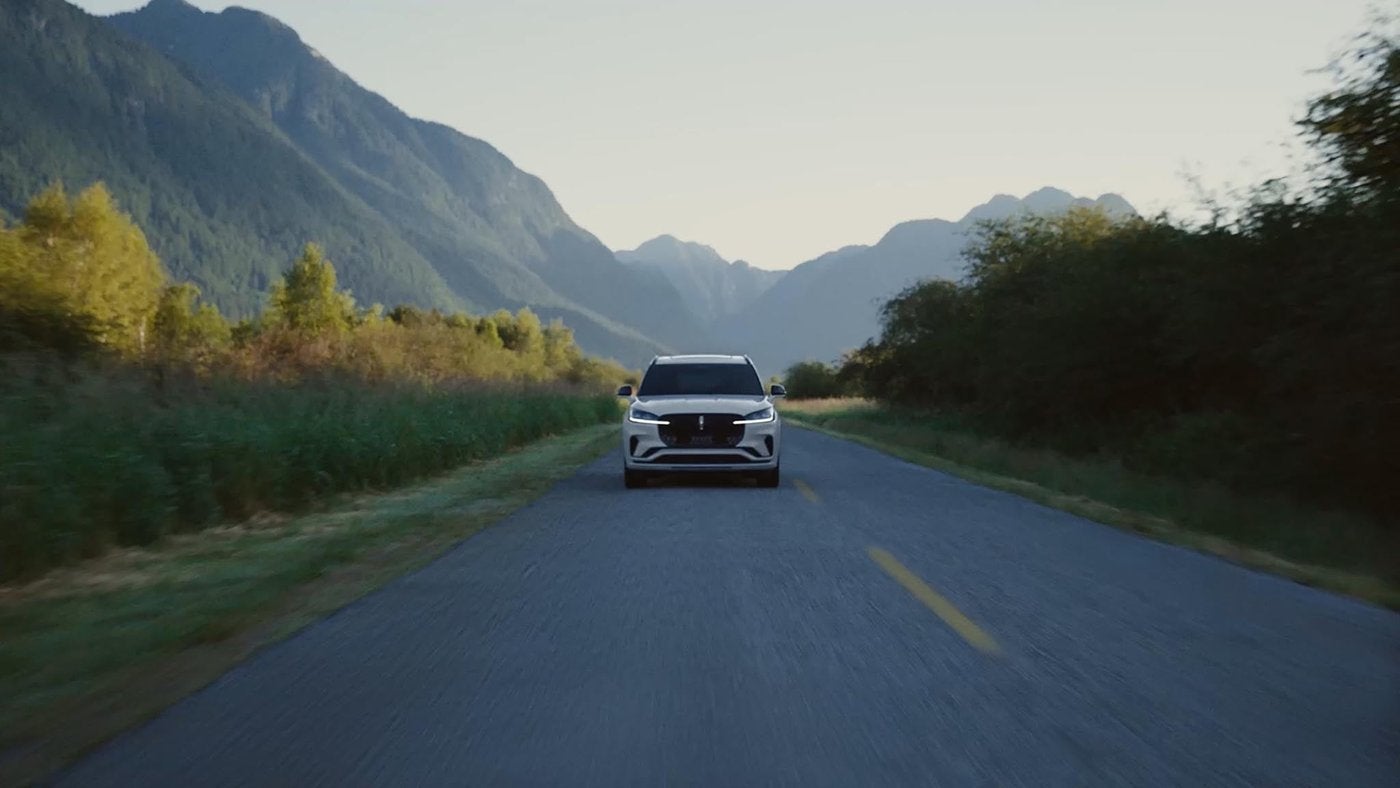 White Lincoln Aviator driving toward the camera on a mountain valley road