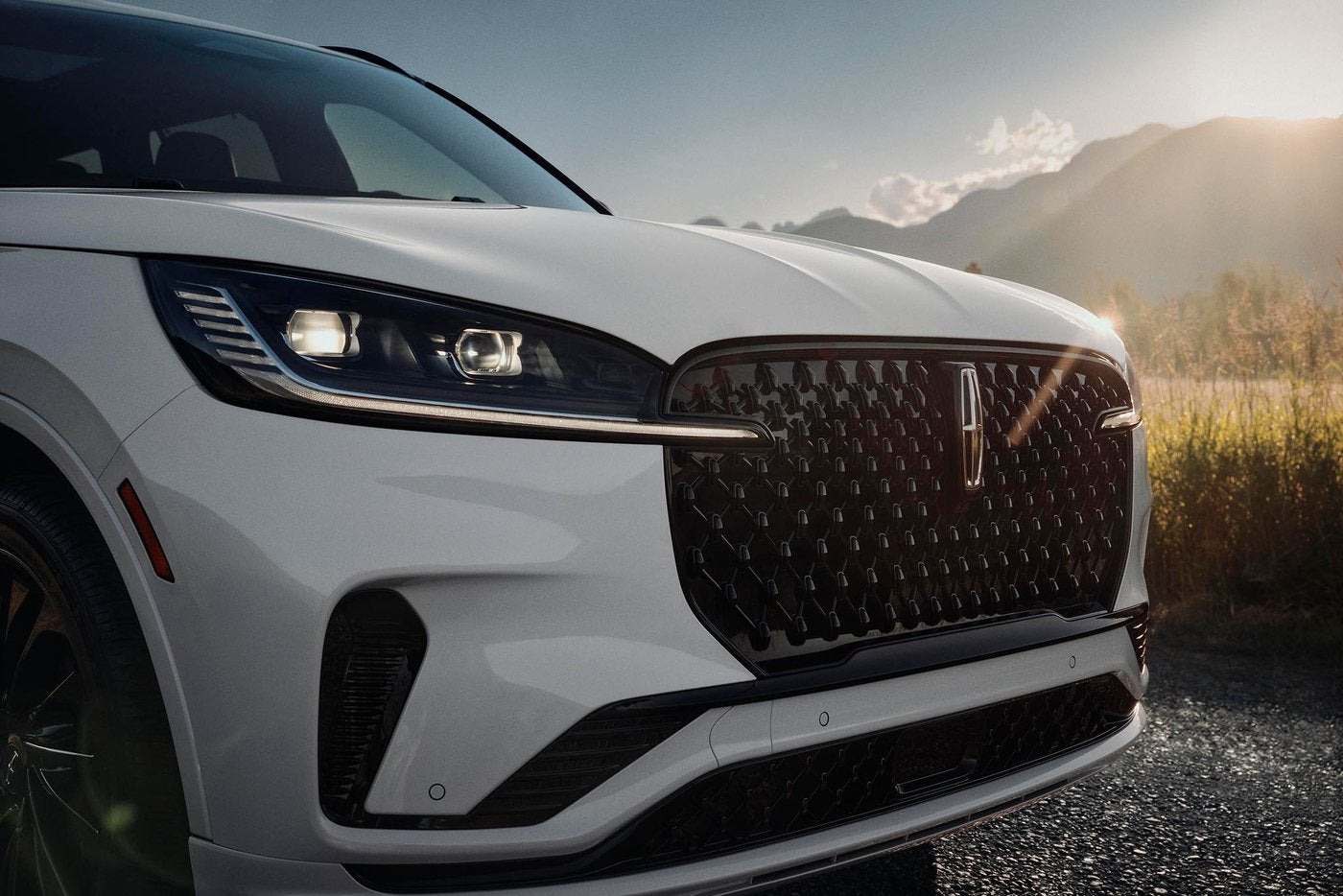 Front of a white Lincoln Aviator with its grille lit and headlights on