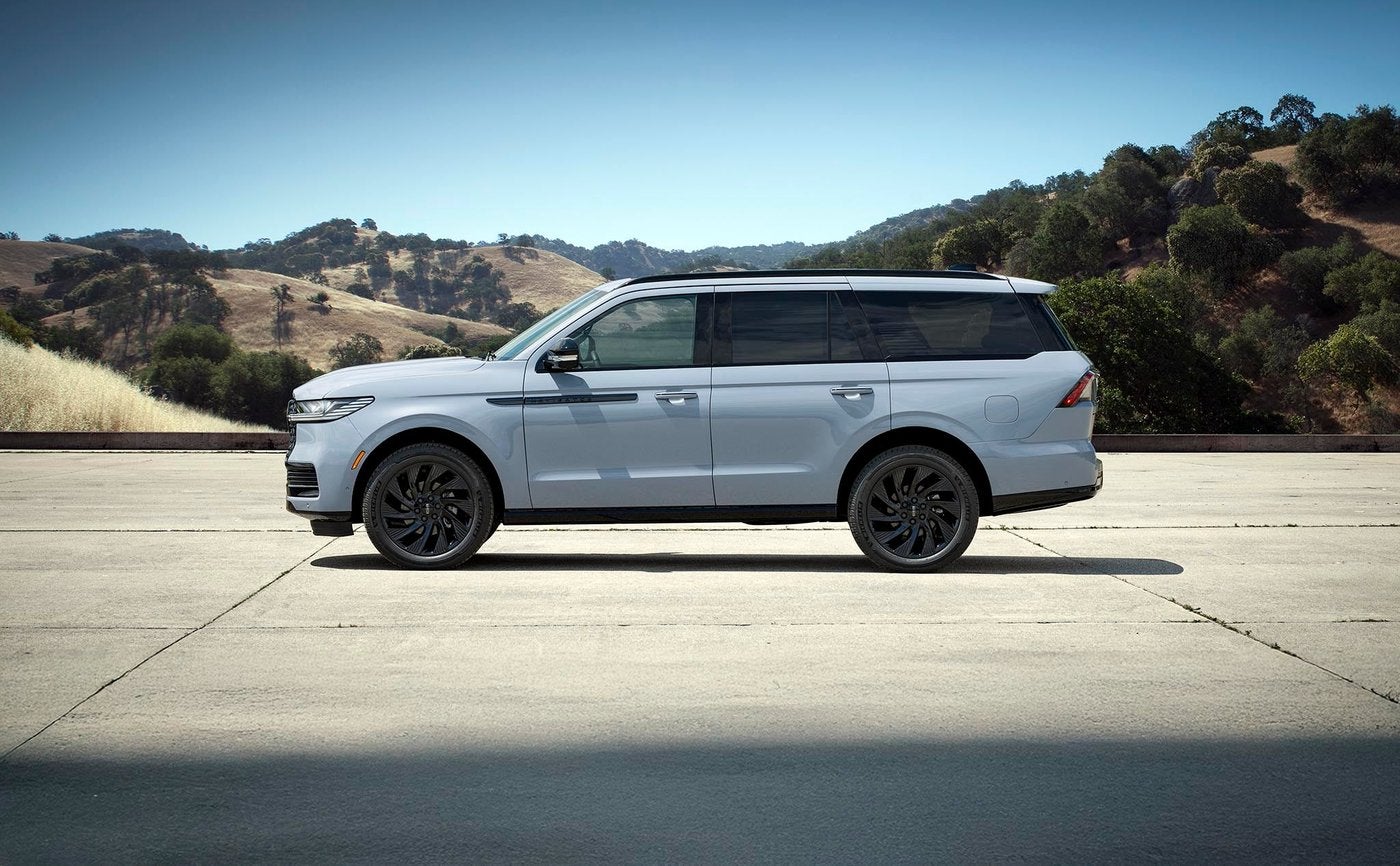Light blue Lincoln Navigator parked on pavement with hills behind it